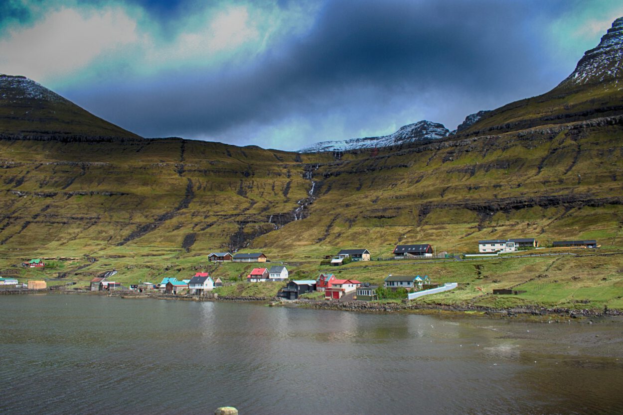 Eine Häusergruppe auf einem Hügel neben einem Gewässer.