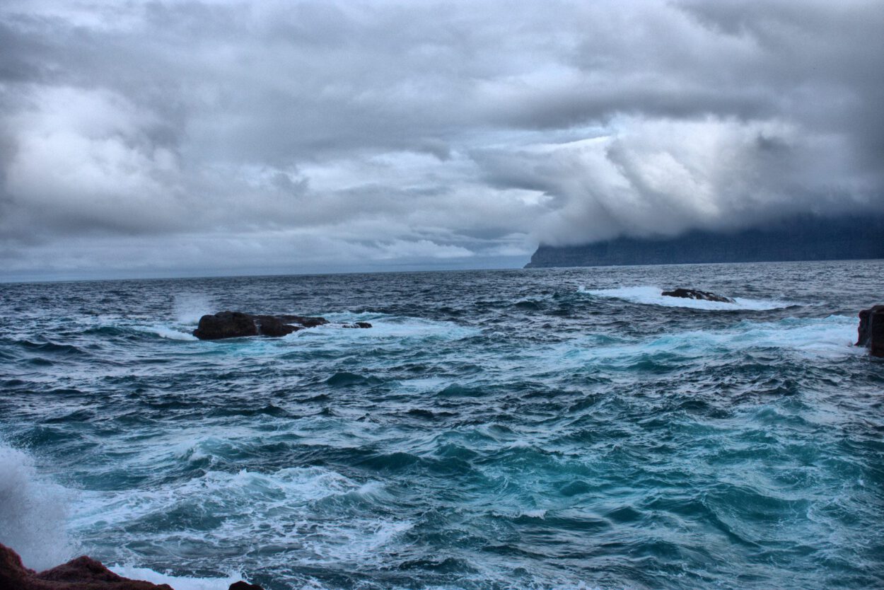 Ein stürmischer Himmel über einem felsigen Ufer mit tosenden Wellen.