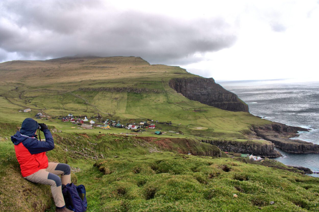Eine Person sitzt auf einem Hügel mit Blick auf den Ozean.