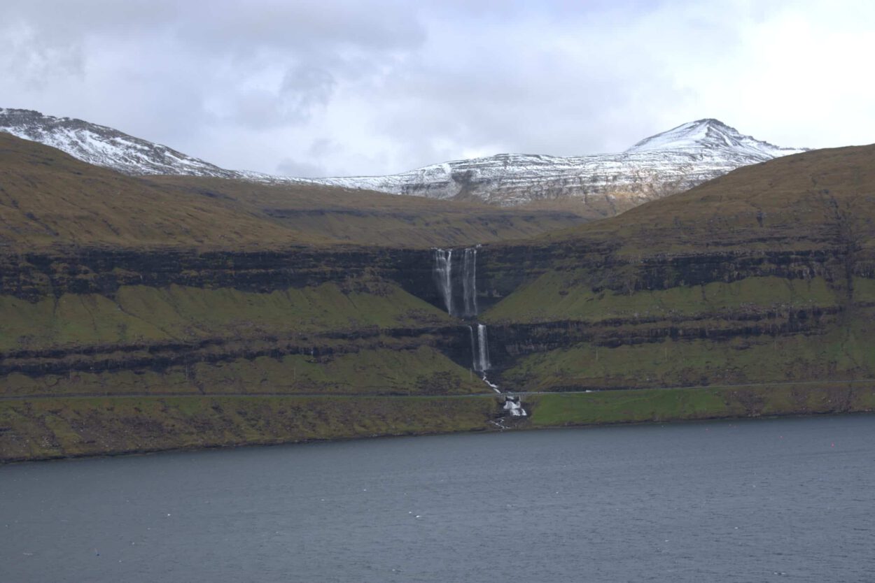 Ein Wasserfall mit einem Berg im Hintergrund.