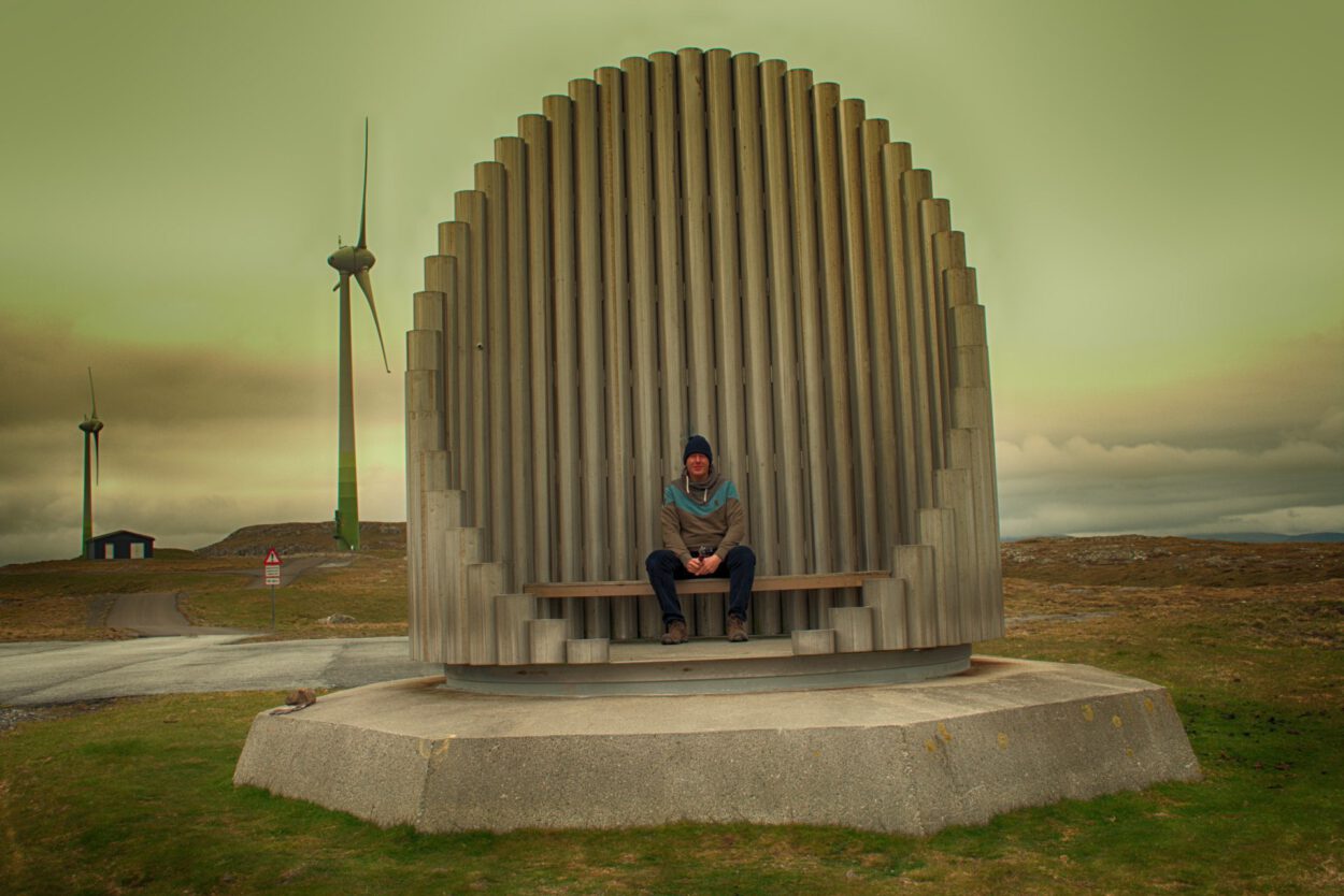 Ein Mann sitzt auf einer Bank vor einer Windkraftanlage.