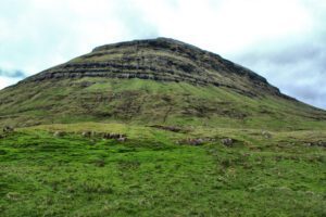 Eine grüne Wiese mit einem Berg im Hintergrund.