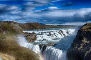 Ein Wasserfall in Island mit einem Regenbogen am Himmel.