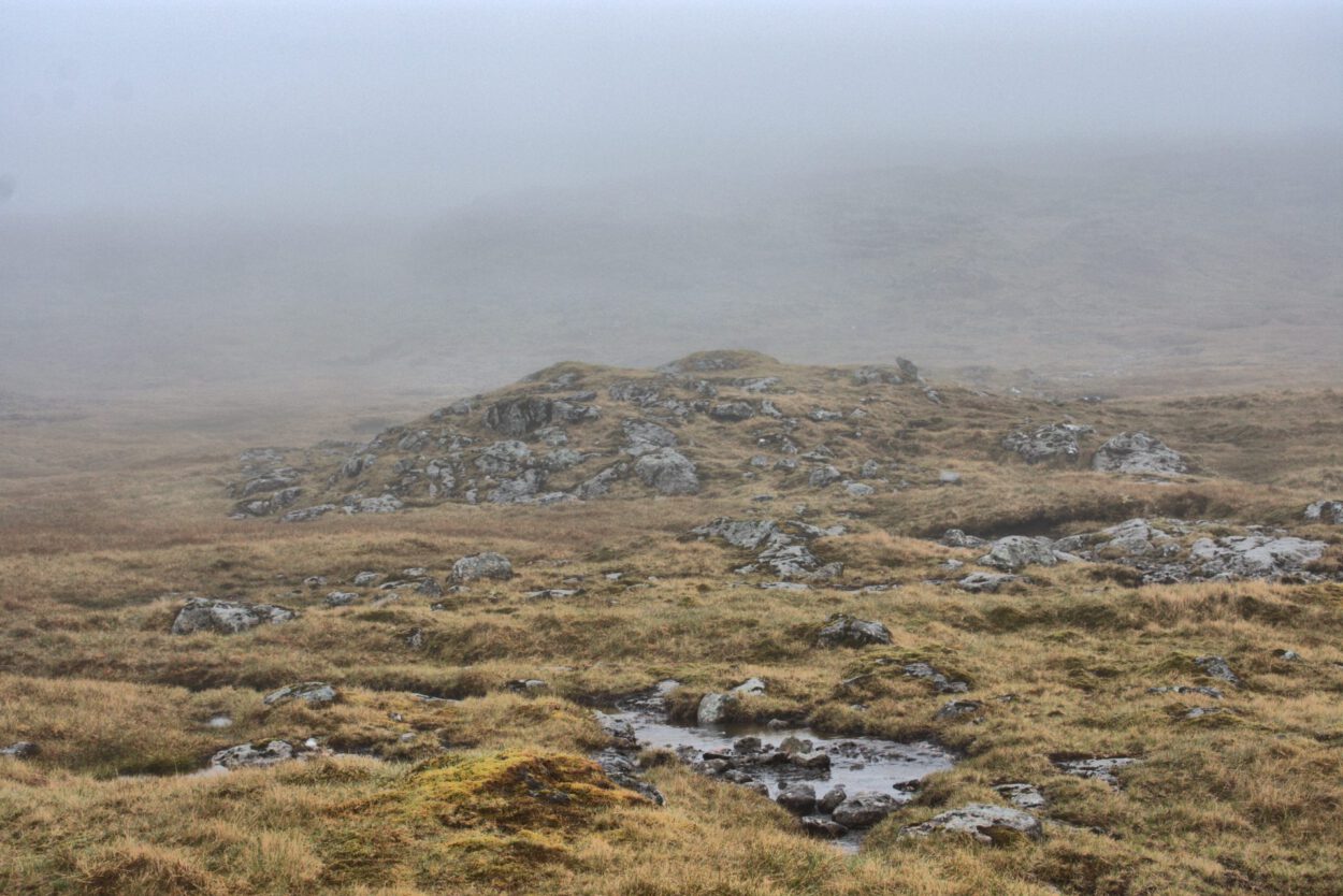 Ein Hügel bedeckt mit Nebel, Gras und Felsen.