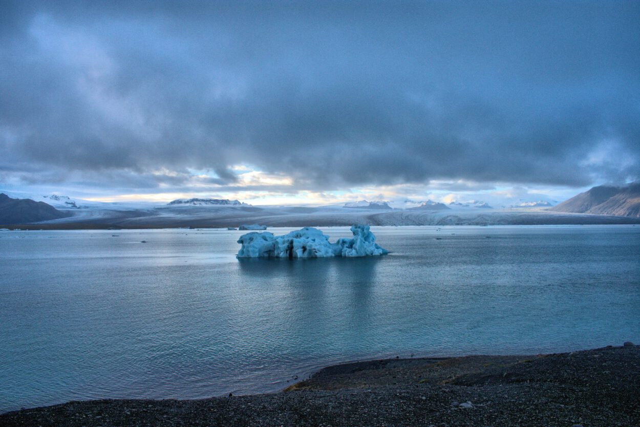 Ein Eisberg in einem Gewässer unter bewölktem Himmel.
