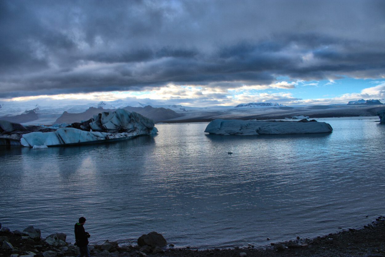 Eine Person steht vor einem Gewässer mit Eisbergen.