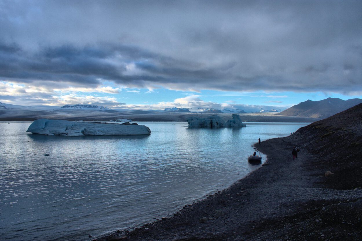 Eine Gruppe von Menschen an einem felsigen Strand neben Eisbergen.