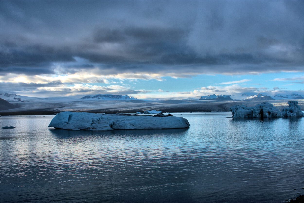 Eisberge schwimmen in einem Gewässer unter bewölktem Himmel.