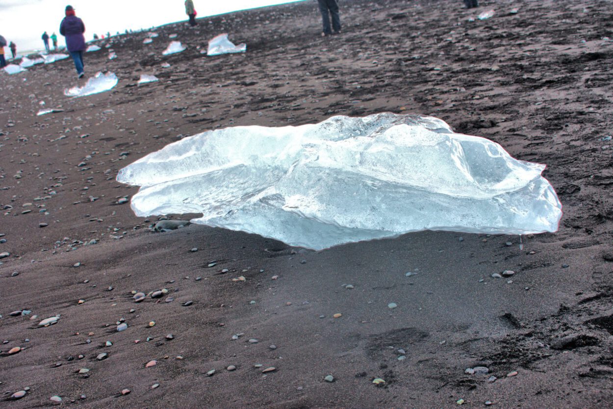 Ein großes Stück Eis liegt an einem schwarzen Sandstrand.