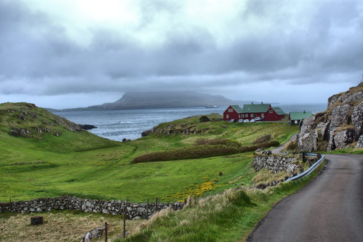 Eine Straße, die zu einem roten Haus an der Küste der Färöer-Inseln führt.