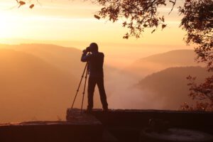 Ein Mann auf einem Stativ fotografiert einen Berg bei Sonnenuntergang.