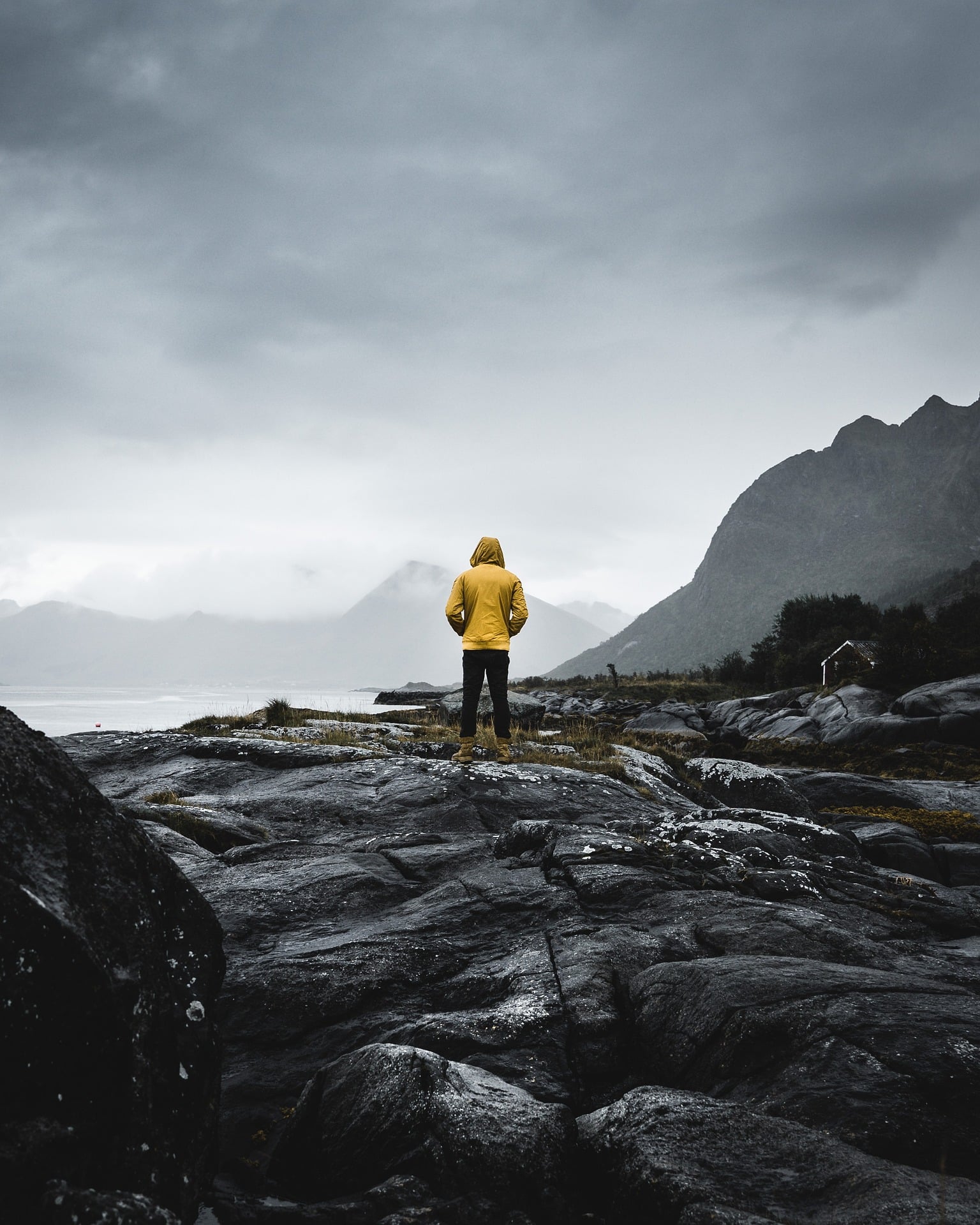 Ein menschen steht auf einen Steinfeld und blickt in die Ferne. Die Person hat eine gelbe Jacke an und ist mit dem Rücken zum Fotografen
