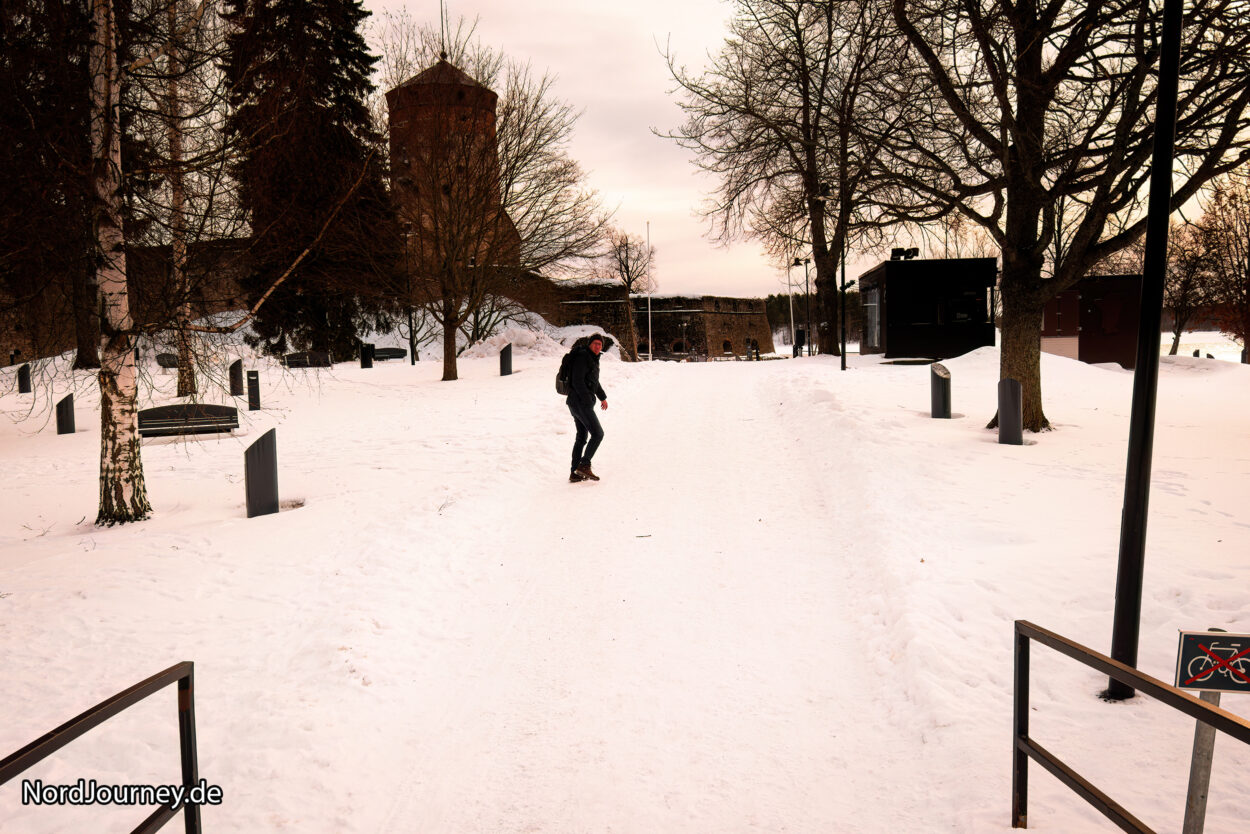 Eine Person fährt mit einem Skateboard einen schneebedeckten Weg entlang.